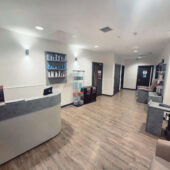 Clean, modern reception area featuring a curved desk, product displays, and treatment rooms in a well-lit corridor.