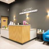 Reception desk at Chilterns Spa & Wellness with a blue sofa and wall lights.