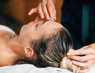 Lady receiving crystal therapy treatment. Crystals placed on forehead and held on the top of her head by the therapist.