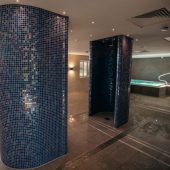 Moulton Spa area. Blue mosaic showers with a spa pool in the background and subtle mood lighting.