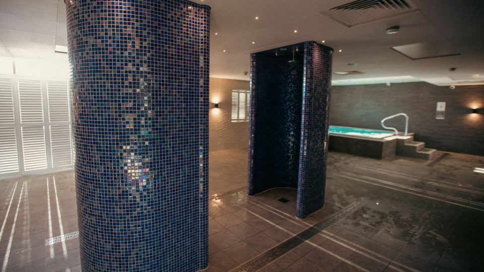 Moulton Spa area. Blue mosaic showers with a spa pool in the background and subtle mood lighting.