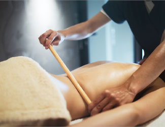 Person receiving a bamboo stick massage on their back in a spa setting.
